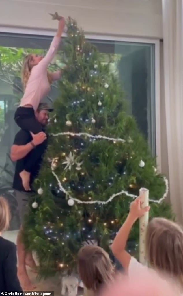 As Elsa struggles to maintain balance, Chris stands on tiptoes, while the glamorous actress pulls the tree toward her so she can reach the tip of it.  Unfortunately for Chris, this tactic comes close to ruining the star's good looks as tree branches crash into his head